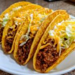 Four crispy hard-shell Cheesy Ground Beef Tacos filled with seasoned meat, topped with shredded cheese, lettuce, and sour cream.