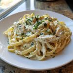 A close-up of a white plate filled with Creamy Alfredo Chicken Pasta Easy Recipe, topped with parsley.