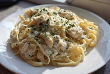 A serving of Creamy Alfredo Chicken Pasta Easy Recipe featuring fettuccine, chunks of chicken, and garnished with parsley.