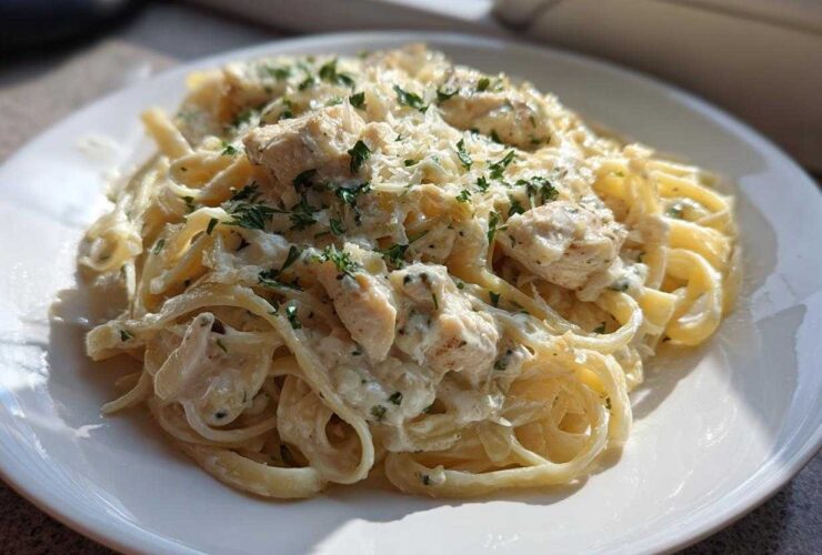 A serving of Creamy Alfredo Chicken Pasta Easy Recipe featuring fettuccine, chunks of chicken, and garnished with parsley.