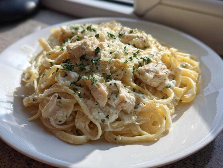 A serving of Creamy Alfredo Chicken Pasta Easy Recipe featuring fettuccine, chunks of chicken, and garnished with parsley.