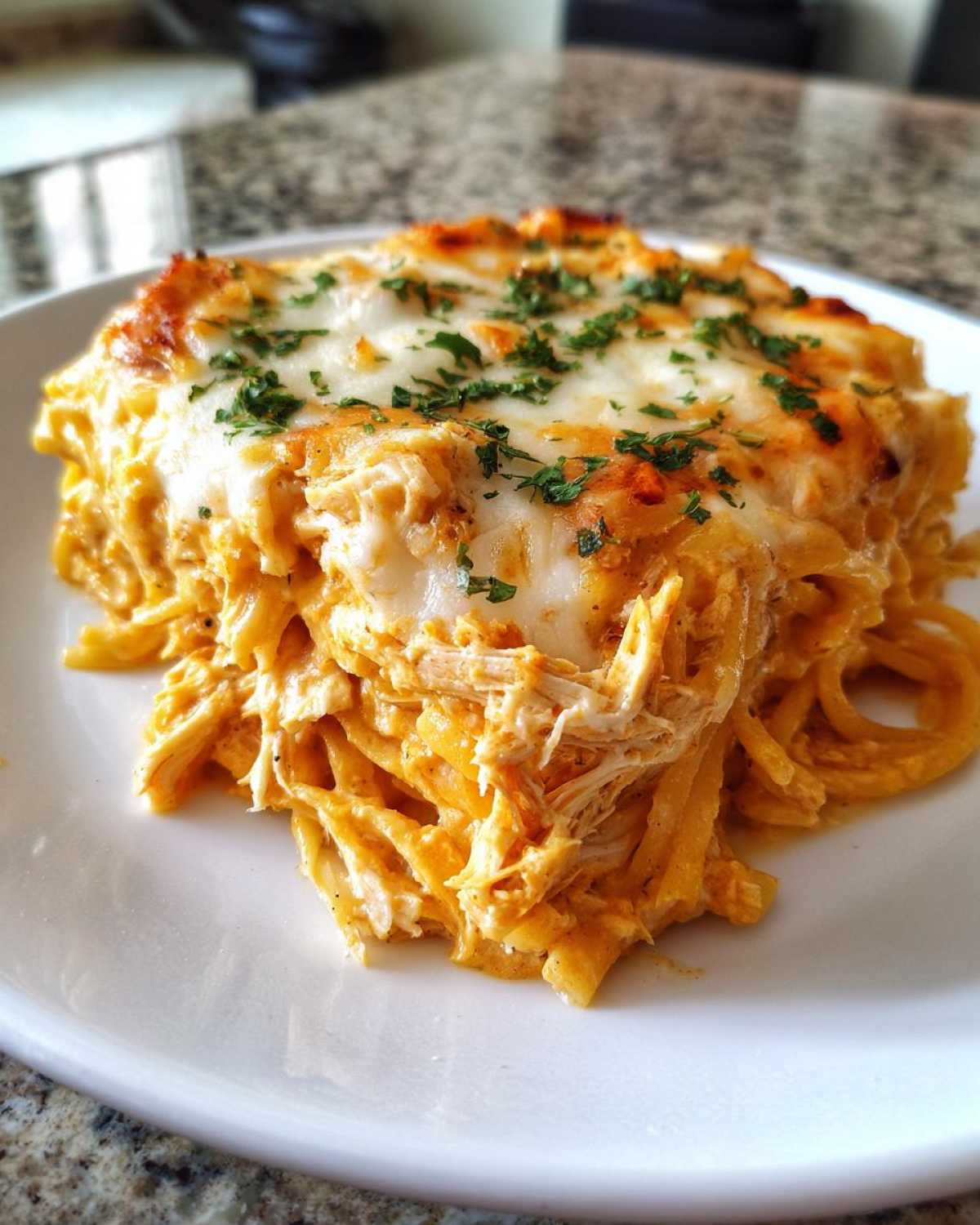 A generous serving of Creamy Cajun Chicken Alfredo Bake, featuring shredded chicken, pasta, and a top layer of melted, browned cheese garnished with parsley.