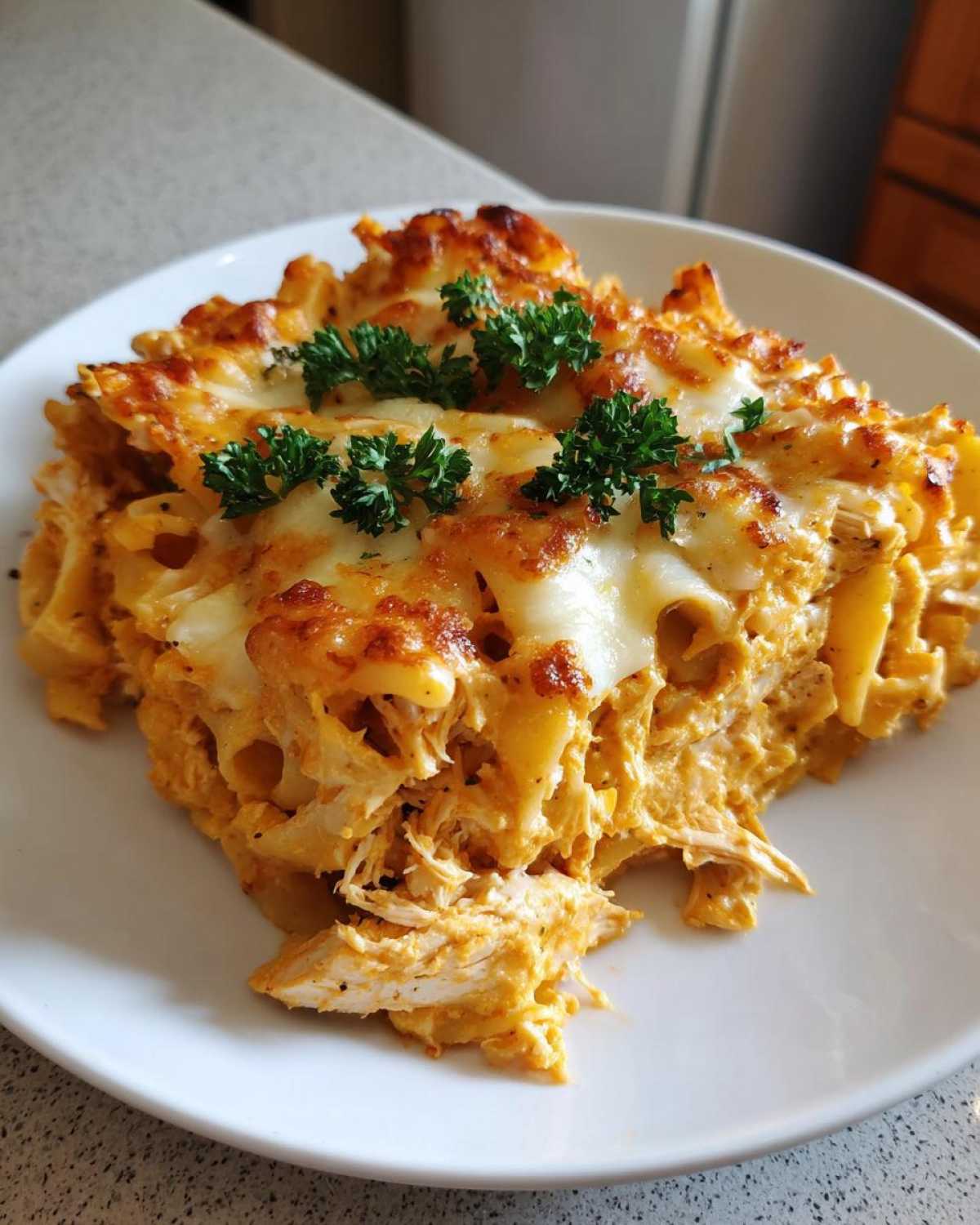 A close-up of a serving of Creamy Cajun Chicken Alfredo Bake, topped with melted, browned cheese and fresh parsley.