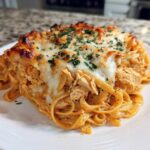 A close-up shot of a serving of Creamy Cajun Chicken Alfredo Bake, featuring fettuccine pasta, shredded chicken, and a bubbly, browned cheese topping.
