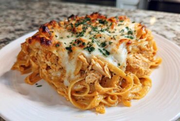 A close-up shot of a serving of Creamy Cajun Chicken Alfredo Bake, featuring fettuccine pasta, shredded chicken, and a bubbly, browned cheese topping.