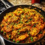 Close-up of vibrant Creamy Cajun Chicken Skillet with Rice, featuring chicken pieces, rice, and bright green peas.