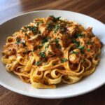 A close-up of fettuccine pasta topped with chunks of chicken in a rich, orange-hued Creamy Cajun Pasta with Chicken and Spice sauce, garnished with parsley.