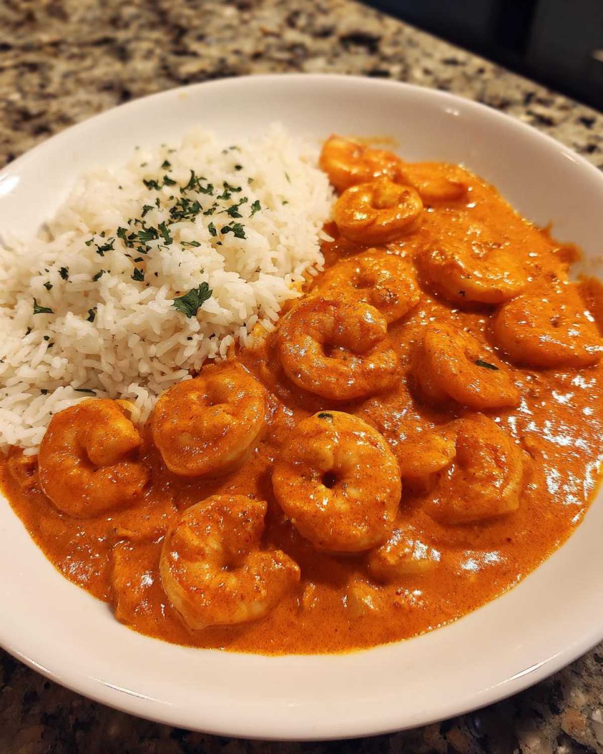 A white bowl filled with Creamy Cajun Shrimp and Rice Skillet, featuring shrimp in a rich orange sauce next to white rice.