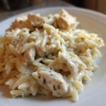 A close-up serving of Creamy Garlic Parmesan Orzo with Chicken coated in a rich white sauce and sprinkled with herbs.