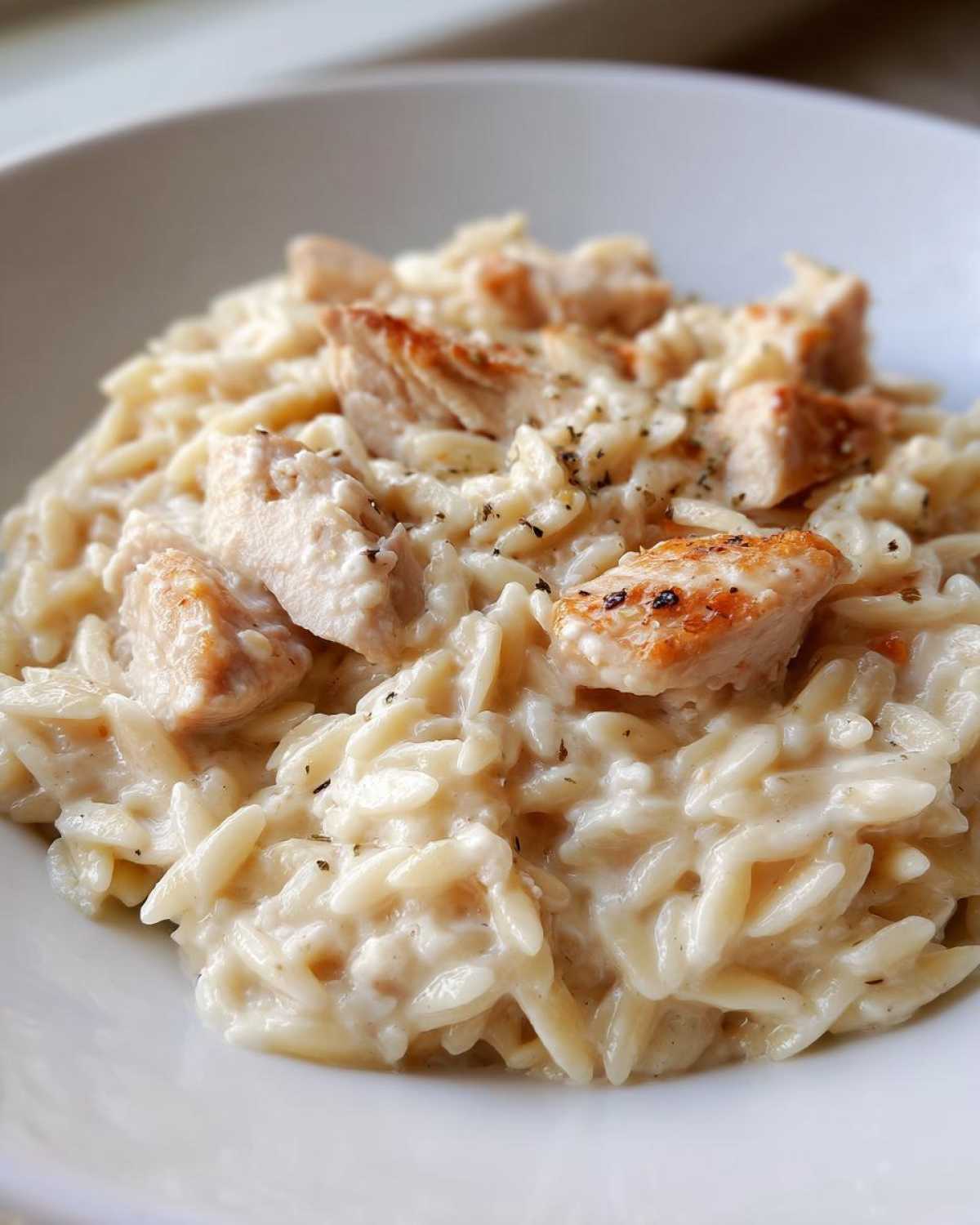 Close-up of a bowl of Creamy Garlic Parmesan Orzo with Chicken topped with seasoned grilled chicken pieces.