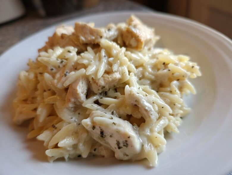 A close-up serving of Creamy Garlic Parmesan Orzo with Chicken coated in a rich white sauce and sprinkled with herbs.