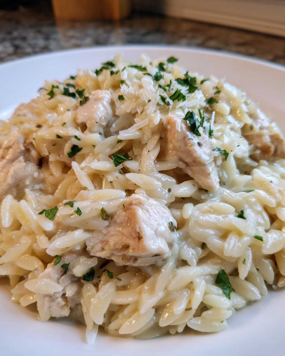 Close-up of creamy garlic parmesan orzo with chicken pieces, topped with grated cheese and fresh parsley.