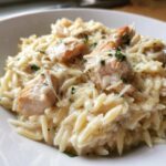 A close-up of creamy garlic parmesan orzo with chicken pieces, topped with shredded cheese and parsley.