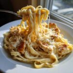 A fork lifting creamy fettuccine noodles showing cheese pull from a plate of Honey Garlic Chicken Pasta with cream sauce.