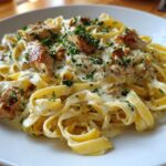 Close-up of fettuccine pasta coated in a rich sauce with chunks of seared chicken, garnished with parsley: Creamy Lemon Garlic Pasta with Chicken.