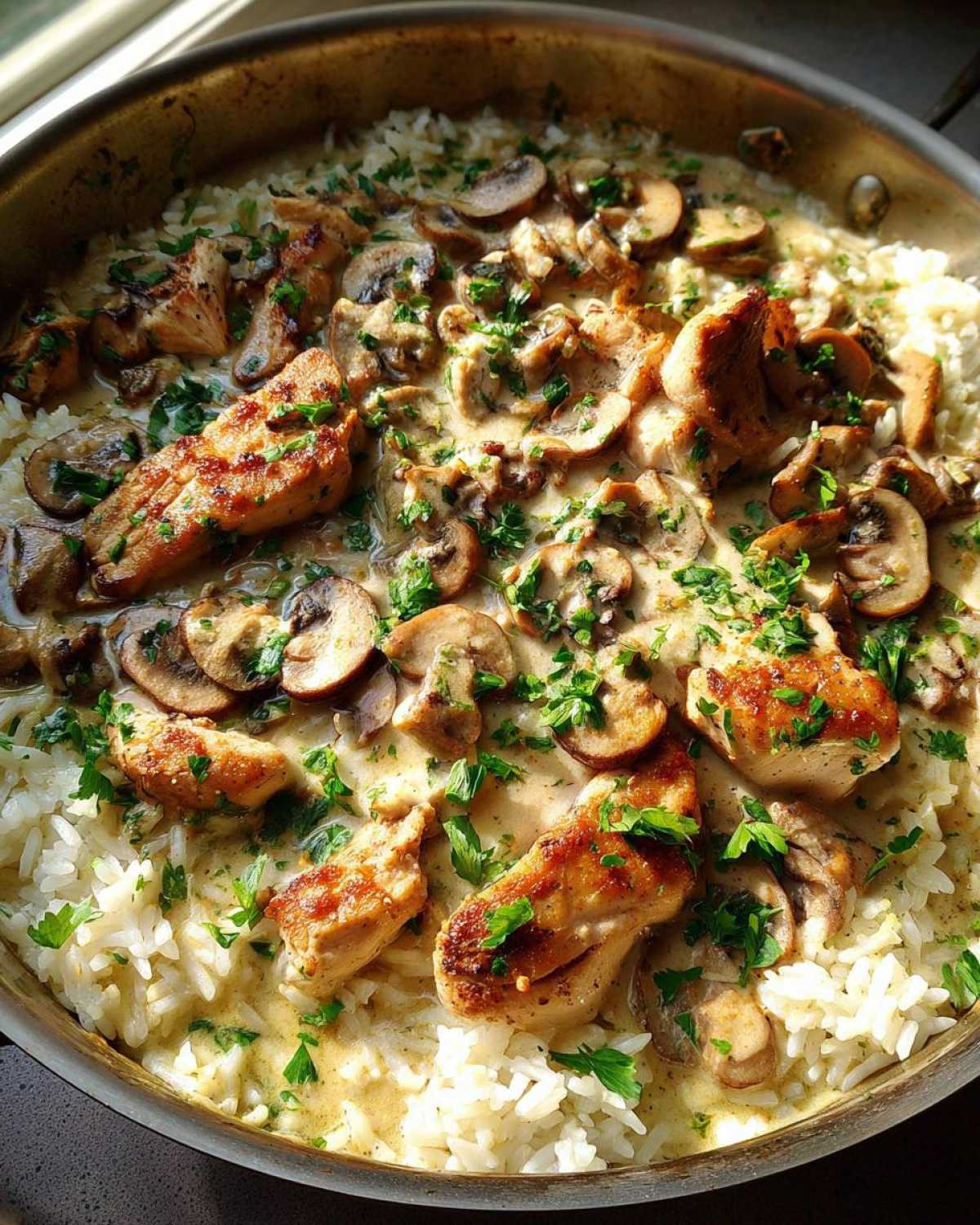 Close-up of Creamy Mushroom Chicken and Rice Skillet garnished with fresh parsley in a metal pan.
