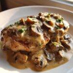 A perfectly cooked chicken breast smothered in a rich sauce with sliced mushrooms, part of the Creamy Mushroom Chicken recipe.