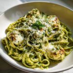 A bowl of Creamy Pesto Chicken Pasta with Mozzarella, topped with grated cheese and fresh mint.