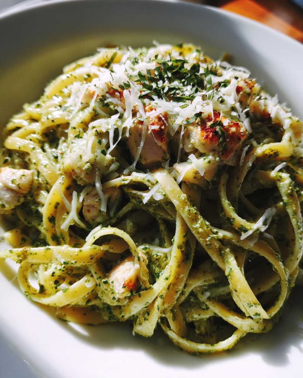 Close-up of creamy pesto chicken pasta with mozzarella shreds and fresh parsley garnish.