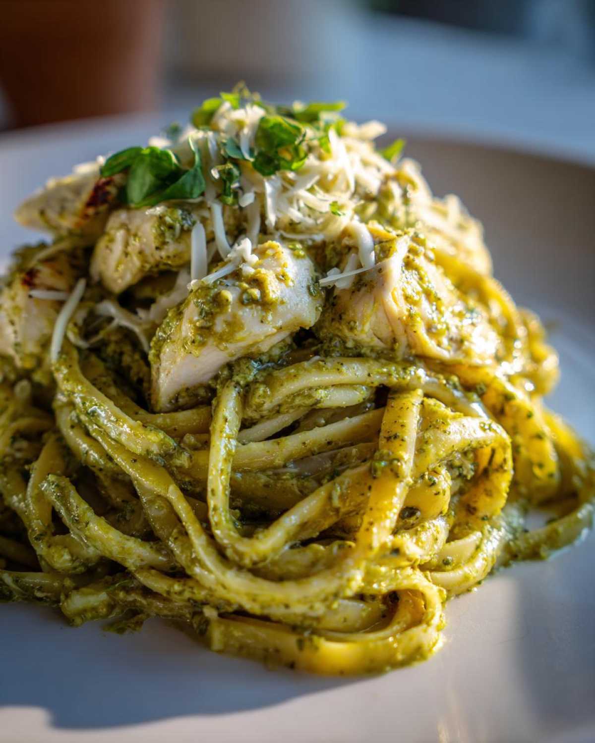 A close-up serving of Creamy Pesto Chicken Pasta with Mozzarella, topped with shredded cheese and fresh basil.