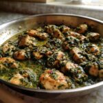 Close-up of seasoned chicken pieces simmering in a rich, green sauce with spinach in a stainless steel skillet, ready for Creamy Spinach Chicken Skillet with Parmesan.