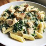 Close-up of a bowl of Creamy Spinach Pasta with Chicken, featuring penne pasta, sautéed spinach, and diced chicken in a rich white sauce.