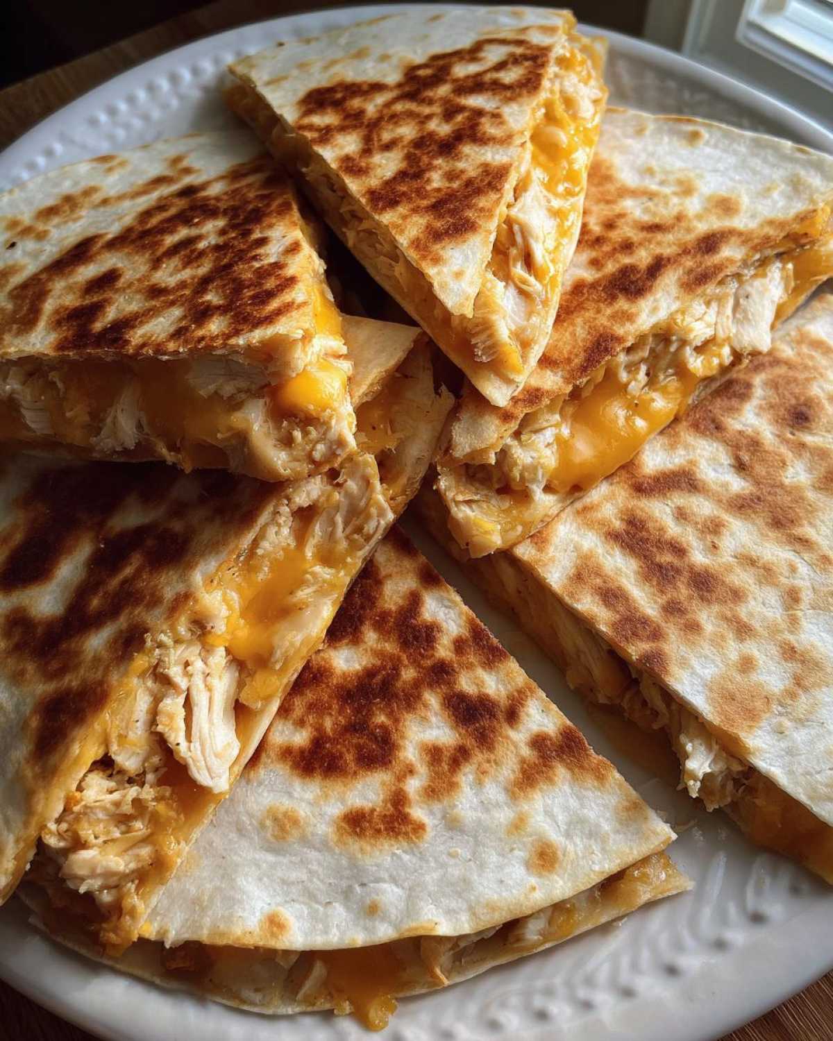 Several wedges of Cheesy Chicken Quesadilla with Crispy Tortilla piled on a white plate, showing melted cheddar cheese and shredded chicken.