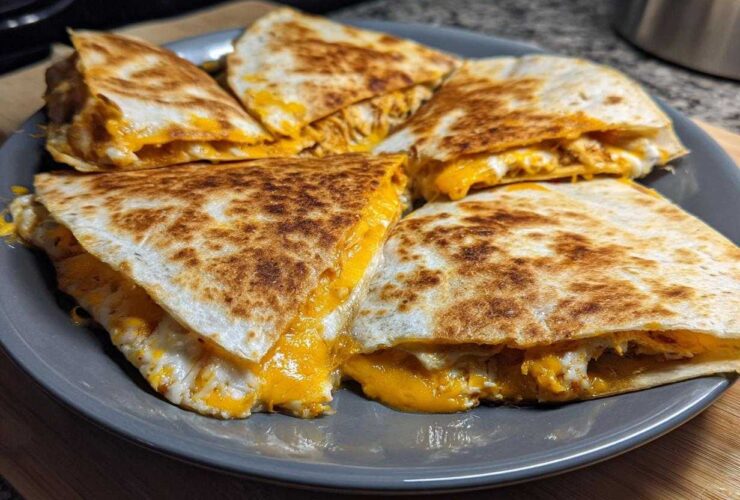 Four wedges of a crispy Cheesy Chicken Quesadilla with melted orange and white cheese spilling out, served on a grey plate.