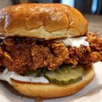A close-up of a Crispy Chicken Sandwich with Garlic Sauce, featuring a thick fried chicken patty, pickles, and a brioche bun.
