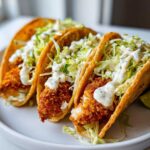 Three crispy chicken tacos filled with crunchy chicken, shredded cabbage, and drizzled with garlic lime sauce.