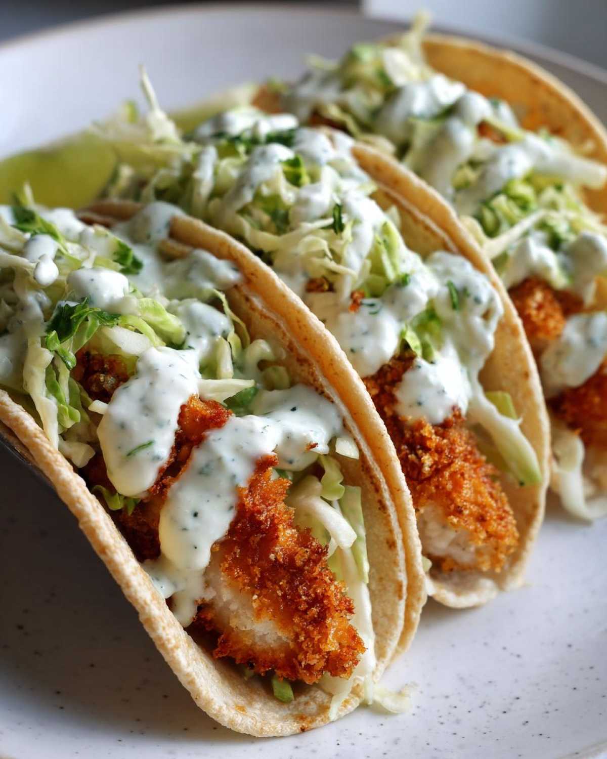 Three Crispy Chicken Tacos topped with shredded cabbage and drizzled generously with Garlic Lime Sauce.