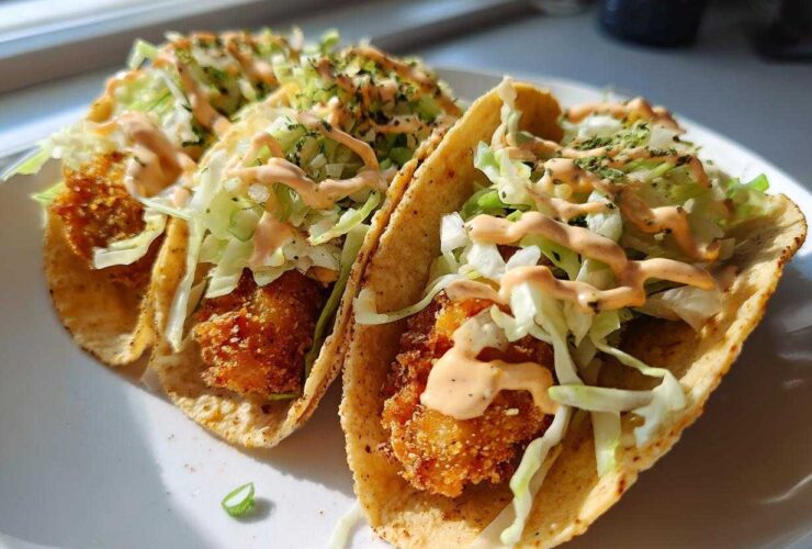 Two crispy chicken tacos topped with shredded lettuce and drizzled with garlic lime sauce.