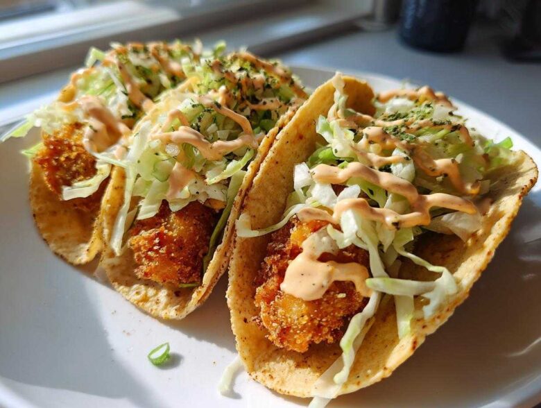 Two crispy chicken tacos topped with shredded lettuce and drizzled with garlic lime sauce.