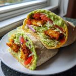 Close-up of a Crispy Chicken Wrap with Avocado Sauce, cut in half, showing crispy chicken, lettuce, tomato, and red onion.