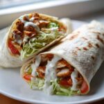 Two halves of a Crispy Chicken Wrap with Creamy Garlic Sauce, filled with lettuce, tomato, and crispy chicken.