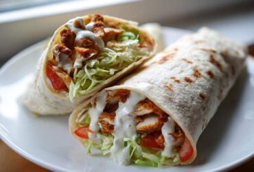 Two halves of a Crispy Chicken Wrap with Creamy Garlic Sauce, filled with lettuce, tomato, and crispy chicken.