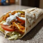 A close-up of a Crispy Chicken Wrap with Garlic Yogurt Sauce, filled with fried chicken, lettuce, and tomato.