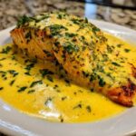 A perfectly cooked salmon fillet generously topped with creamy lemon sauce and fresh herbs, ready to eat.