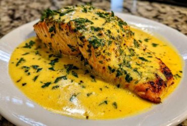 A perfectly cooked salmon fillet generously topped with creamy lemon sauce and fresh herbs, ready to eat.
