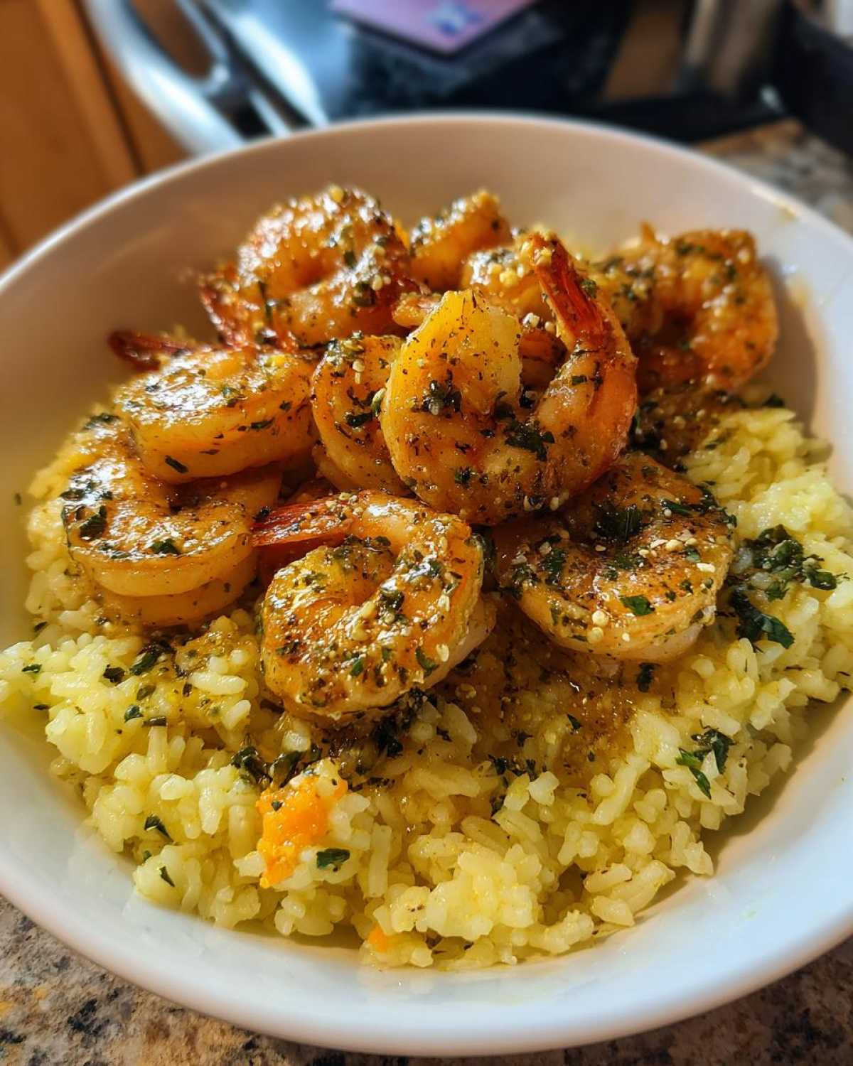 Close-up of a Garlic Butter Shrimp Bowl featuring plump shrimp coated in herbs served over yellow seasoned rice.