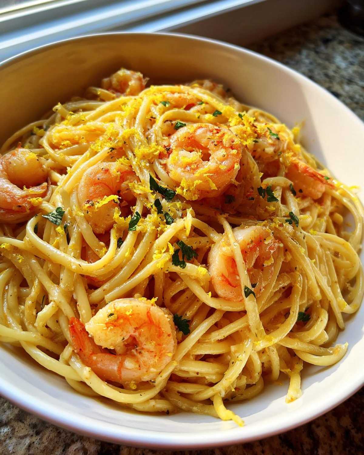 Close-up of a white bowl filled with Garlic Butter Shrimp Pasta with Lemon Flavor, topped with bright lemon zest.