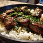 Close-up of seared steak bites served over white rice in a skillet, topped with garlic butter sauce and fresh parsley for Garlic Butter Steak and Rice Skillet Dinner.
