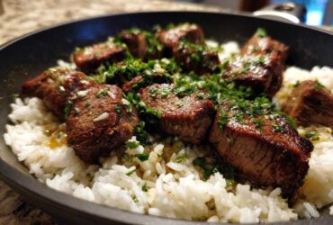 Close-up of seared steak bites served over white rice in a skillet, topped with garlic butter sauce and fresh parsley for Garlic Butter Steak and Rice Skillet Dinner.
