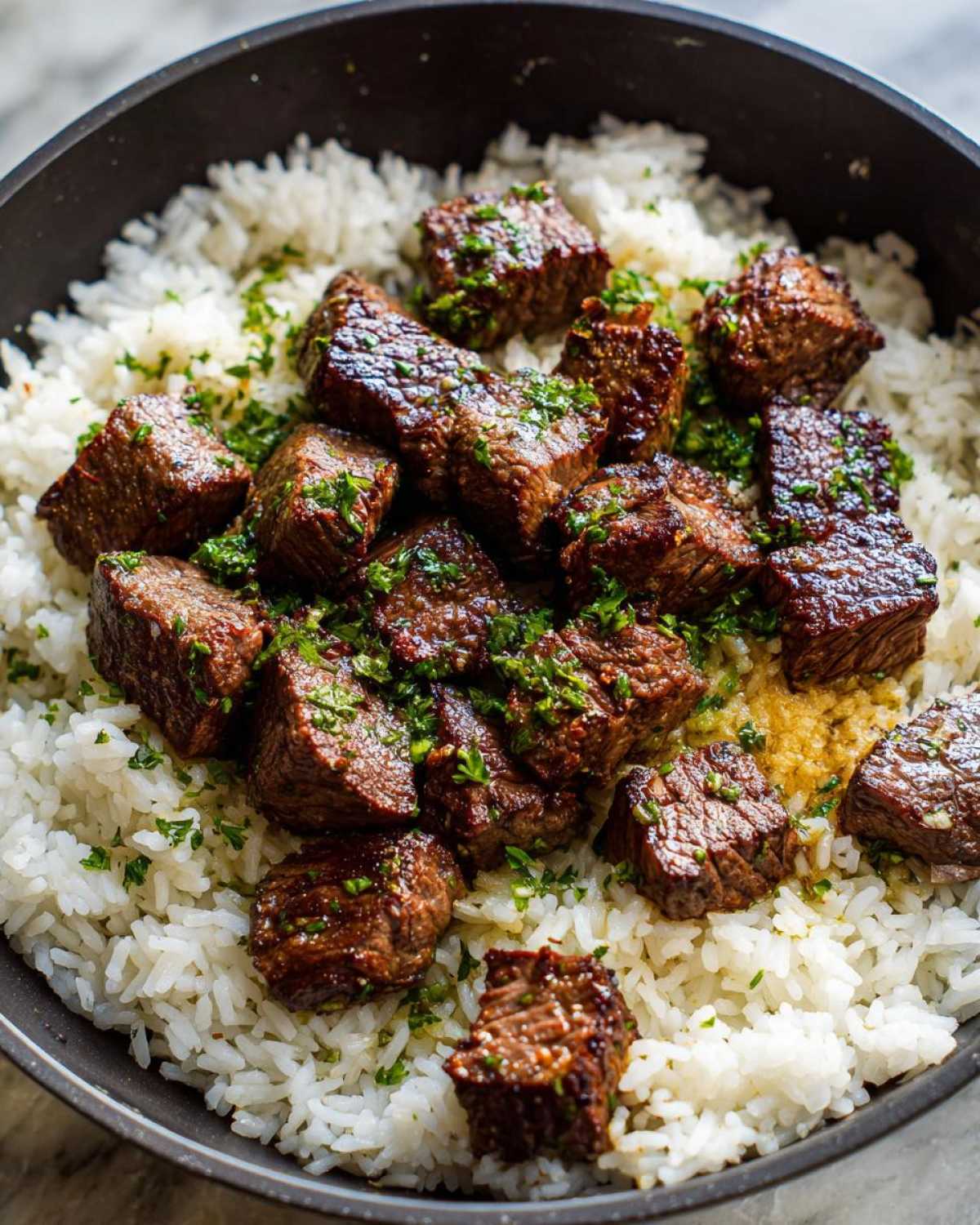 Close-up of seared steak bites served over fluffy white rice in a skillet, drizzled with garlic butter and parsley for a Garlic Butter Steak and Rice Skillet Dinner.