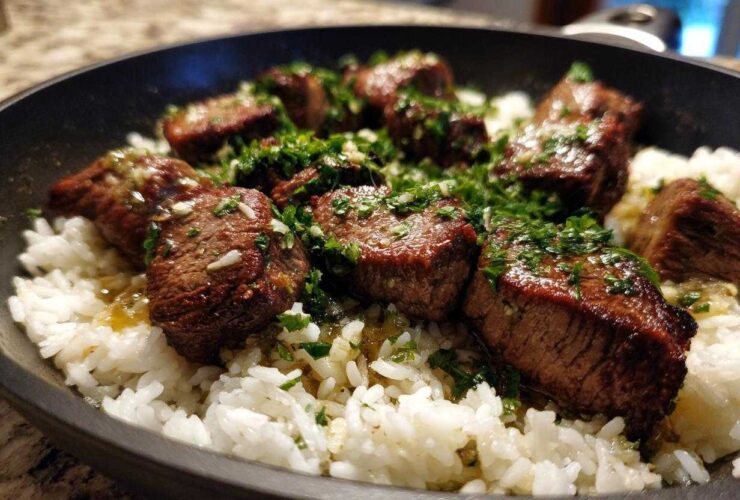 Close-up of seared steak bites served over white rice in a skillet, topped with garlic butter sauce and fresh parsley for Garlic Butter Steak and Rice Skillet Dinner.