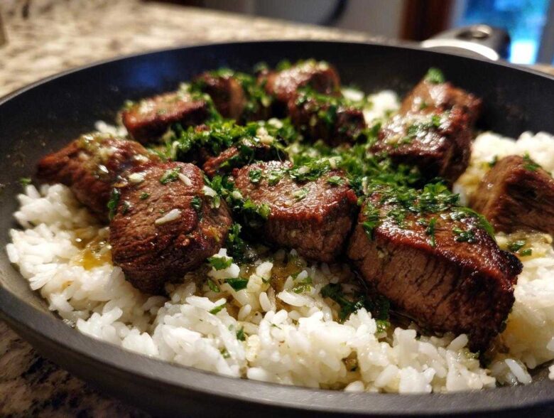 Close-up of seared steak bites served over white rice in a skillet, topped with garlic butter sauce and fresh parsley for Garlic Butter Steak and Rice Skillet Dinner.