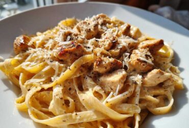 Close-up of Honey Garlic Chicken Pasta with fettuccine noodles in a rich cream sauce, topped with chicken pieces and grated cheese.