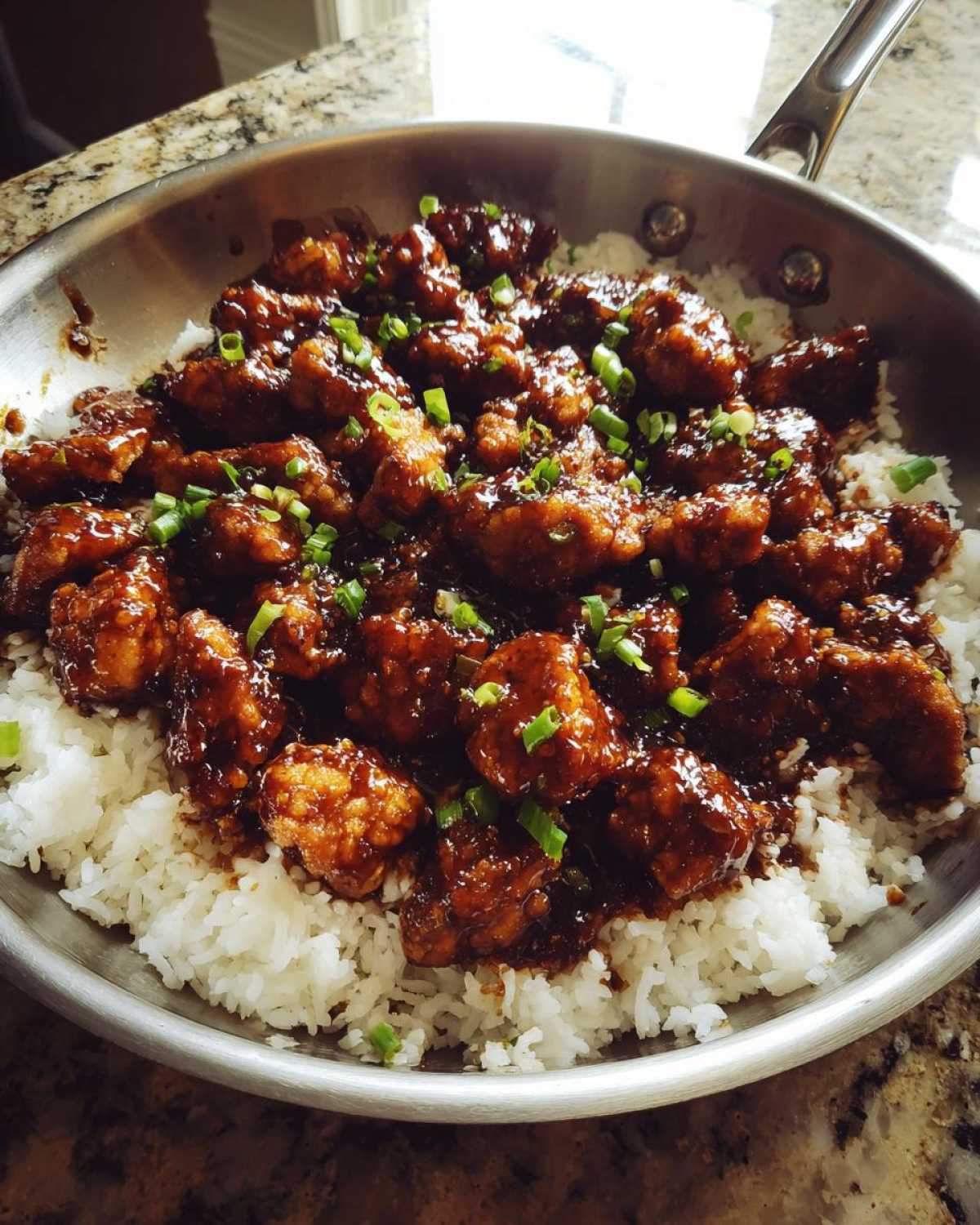 Close-up of Honey Garlic Chicken Skillet with Rice, featuring glazed chicken pieces over white rice in a stainless steel skillet, topped with green onions.