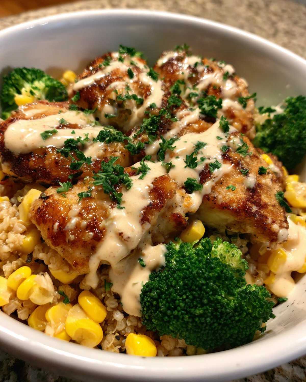 Close-up of a Honey Mustard Chicken Bowl featuring crispy chicken pieces drizzled with creamy sauce over quinoa, corn, and broccoli.