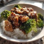 A close-up of a Honey Soy Chicken Bowl Quick Dinner Idea featuring glazed chicken pieces over white rice and bright green broccoli florets, topped with sesame seeds.
